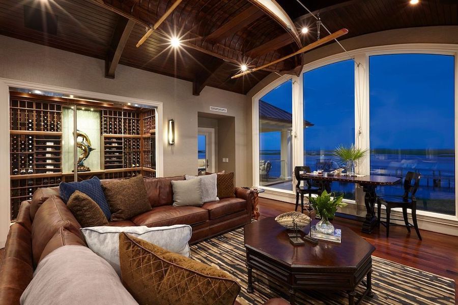 Living area with a brown leather sectional, a brown coffee table, a dining table by a floor-to-ceiling window, and in-ceiling light fixtures.