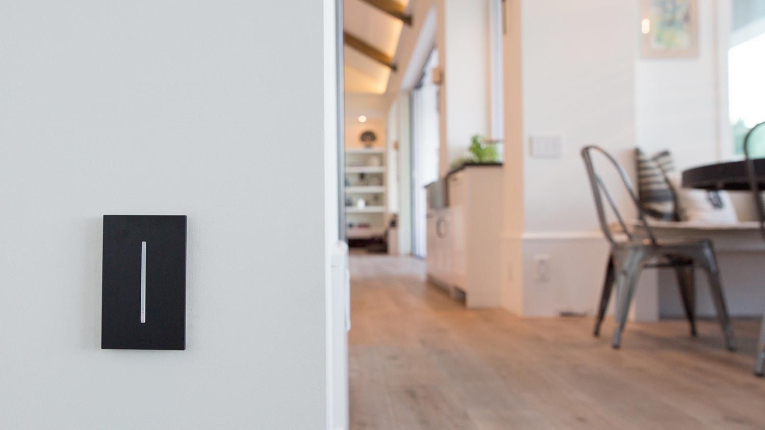 Minimalist black touch-sensitive Lutron light switch on a white wall in a bright, modern home.