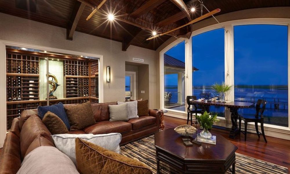 Living area with a brown leather sectional, a brown coffee table, a dining table by a floor-to-ceiling window, and in-ceiling light fixtures.